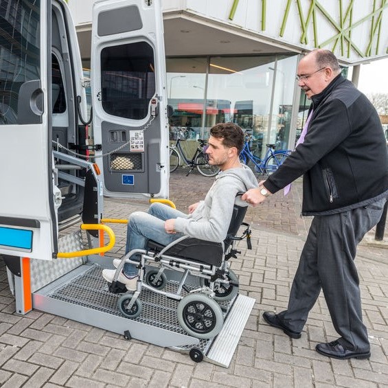 Taxi Driver Assisting Man On Wheelchair To Board Van